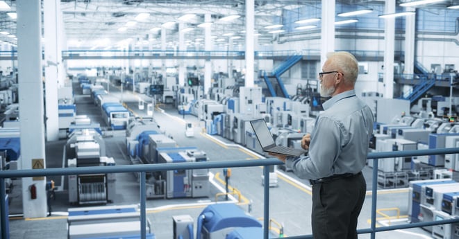 Experienced Male Engineer Standing on a Platform, Using Laptop Computer and Overlooking Production at a Modern Automated Electronics Manufacture with AI Support. Factory Executive at Work
