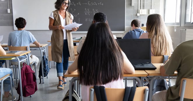 Mature caucasian female teacher handing out exams to multiracial high school students. Students ready to take exam. Education concept.
