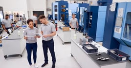 Engineers Meeting On Factory Floor Of Busy Engineering Workshop