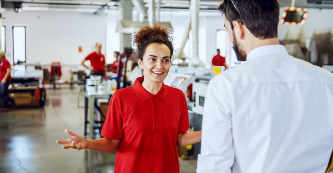 Smiling Caucasian female employee with curly hair talking to her director while standing in printing shop.