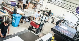 In a large modern printing plant, operators work on various types of machines for printed material