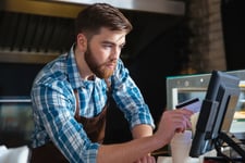 Concentrated-bearded-waiter-swiping-credit-card-through-computer-terminal-in-cafe.jpg