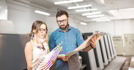 Young woman designer and print operator working together with color swatches standing at the print manufacturing