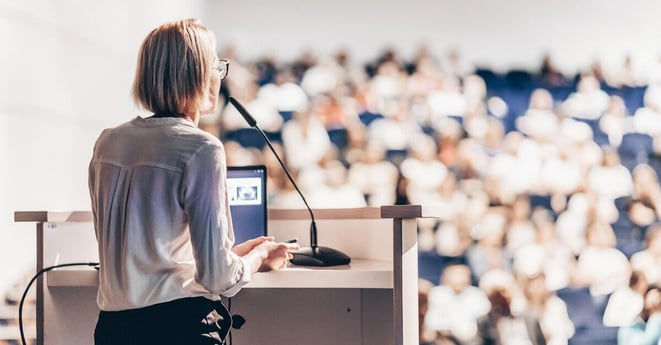 Female speaker giving a talk on corporate business conference. Unrecognizable people in audience at conference hall. Business and Entrepreneurship event