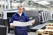 Offset printing. A printer with a printout sheet is standing in front of the printing machine.