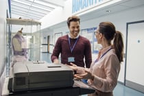 Two teachers are talking while standing at a printer in the school hall. 
