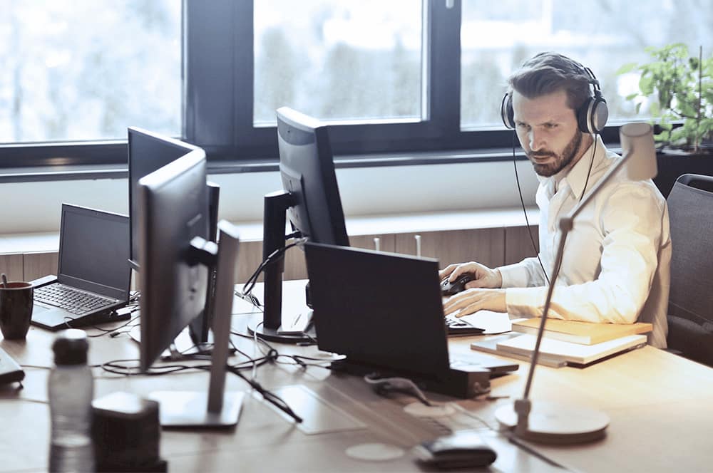 man-working-on-computer-with-headphones-and-monitor